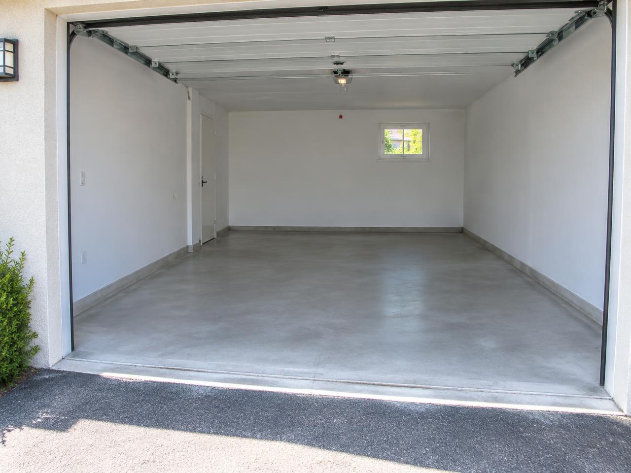 Garage de maison parfaitement dégagé, sol balayé, prêt à accueillir un véhicule